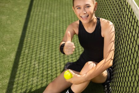 Téléchargez les photos : Joueur de tennis Padel avec raquette. Heureuse athlète fille souriante avec les pouces vers le haut sur le terrain à l'extérieur. Concept sportif. Téléchargez une photo de haute qualité pour la conception d'une application sportive ou d'un site Web - en image libre de droit