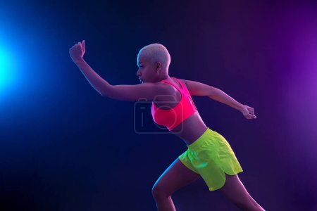 Téléchargez les photos : Une athlète forte, femme sprinteuse, courir sur fond noir vêtue de vêtements de sport, de fitness et de motivation sportive. Concept Runner avec espace de copie - en image libre de droit