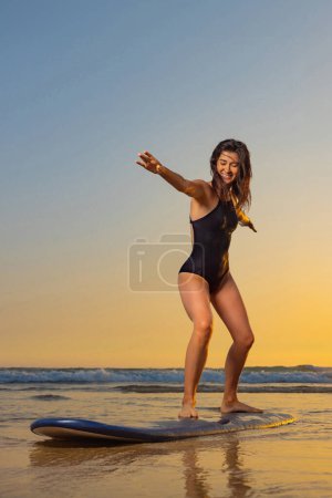 Téléchargez les photos : Surfeuse aux cheveux longs va surfer. Femme tenant une planche de surf sur une plage au coucher du soleil ou au lever du soleil. Surfeur et océan. - en image libre de droit