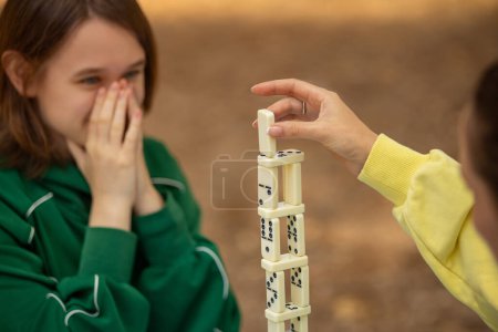 Domino game. Happy family playing board games outdoors in the park. Mom and teen girl playing domino