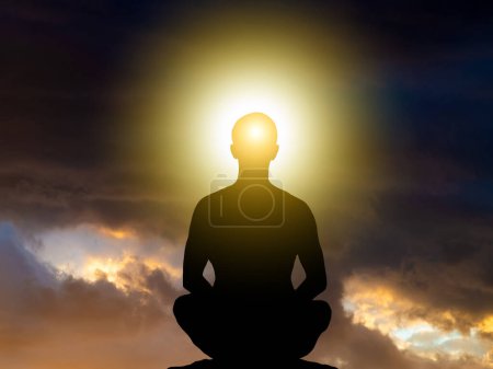 Téléchargez les photos : Silhouette d'un homme assis en position lotus en méditation.Ciel dramatique avec des nuages orageux. - en image libre de droit