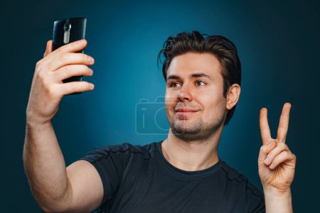 Téléchargez les photos : Jeune homme faisant selfie avec signe de victoire - en image libre de droit