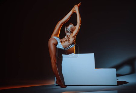Photo for Young slim woman gymnast stretching in studio on dark background - Royalty Free Image