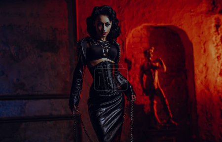 Téléchargez les photos : Jeune femme sexy de style rétro en vêtements noirs posant sur le mur avec fond de lumière rouge - en image libre de droit
