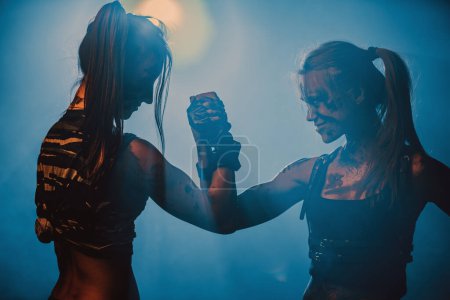 Foto de Dos mujeres luchadoras estrechando las manos en el interior oscuro con humo, tatuaje en el cuerpo - Imagen libre de derechos