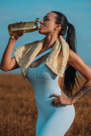 Téléchargez les photos : Jeune femme sportive debout avec bouteille d'eau après l'entraînement, tatouage sur le corps - en image libre de droit