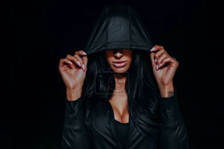 Téléchargez les photos : Jeune femme brune sexy dans le capot sombre portrait de nuit, tatouage à portée de main - en image libre de droit