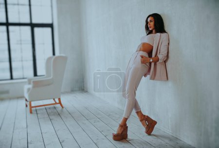 Foto de Joven mujer de estilo empresarial de pie en la pared en el interior blanco suave - Imagen libre de derechos