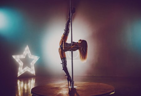 Photo for Young sexy woman in black lingerie pole dancing in dark interior - Royalty Free Image