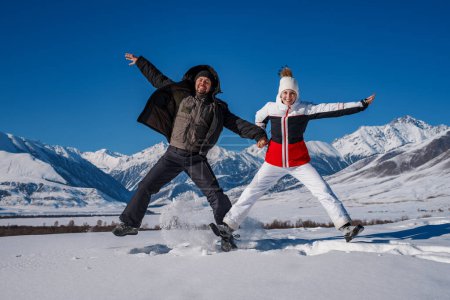 Foto de Joven feliz hombre y mujer saltando en las montañas de fondo en la temporada de invierno - Imagen libre de derechos