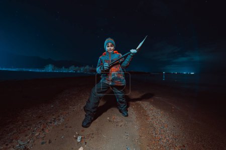 Photo for Child with shovel standing on lake shore at night in heroic pose - Royalty Free Image