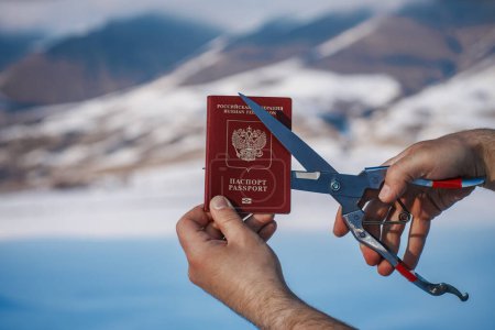 Téléchargez les photos : Homme coupant passeport russe sur fond de montagnes, concept d'immigration - en image libre de droit