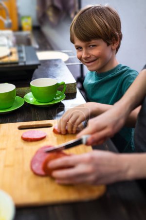 Téléchargez les photos : Un enfant rusé vole de la nourriture de la table de cuisine lorsque la mère cuisine - en image libre de droit