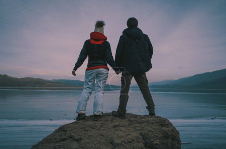 Téléchargez les photos : Homme et femme tenant la main sur fond de lac gelé, couleurs de style rétro foncé - en image libre de droit