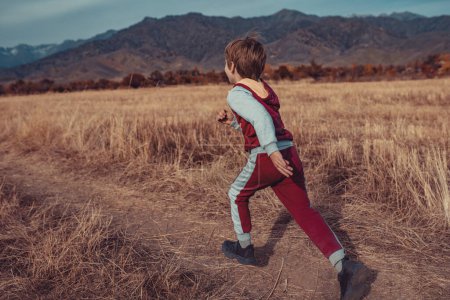 Téléchargez les photos : Enfant courant sur le champ d'automne sur fond de montagnes - en image libre de droit