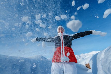 Téléchargez les photos : Jeune femme heureuse jeter de la neige sur fond de montagnes d'hiver - en image libre de droit