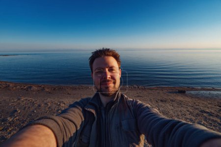 Téléchargez les photos : Jeune homme heureux selfie en face du lac, grand angle de vue - en image libre de droit