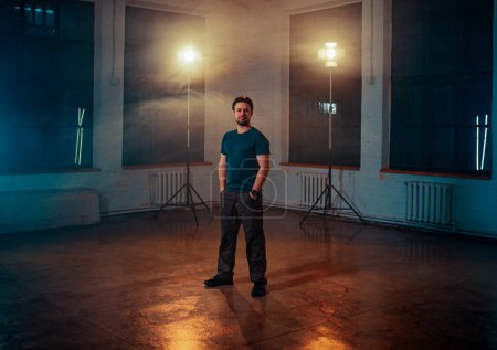 Téléchargez les photos : Jeune homme réalisateur posant dans un studio photo avec une lumière constante - en image libre de droit