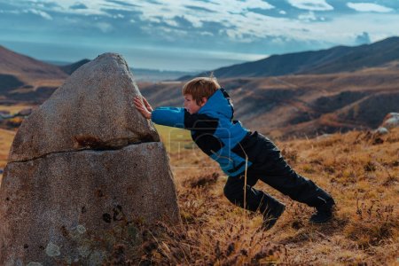 Photo for Boy is trying to move a big stone in the mountains - Royalty Free Image
