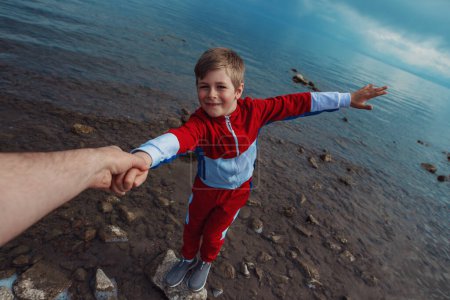 Téléchargez les photos : Père tend la main à son fils debout sur une pierre dans l'eau - en image libre de droit