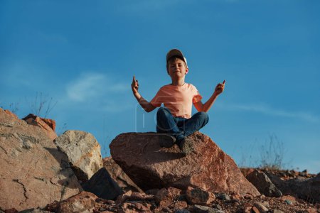 Photo for Boy sitting in meditation pose on rock in the mountains - Royalty Free Image