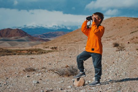 Photo for Boy tourist looking in binoculars in mountains - Royalty Free Image