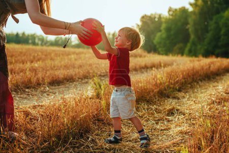 Photo for Young mother gives the ball to her two-year-old son in a field - Royalty Free Image