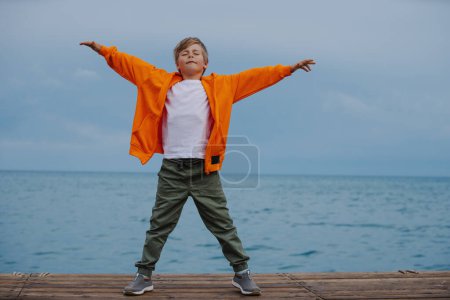 Foto de Niño feliz de pie en la orilla del lago con los brazos extendidos a los lados - Imagen libre de derechos