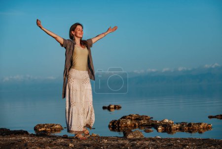 Téléchargez les photos : Belle jeune femme debout les yeux fermés sur la rive du lac - en image libre de droit