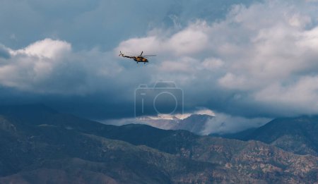 Photo for Military helicopter in the sky over the mountains in cloudy weather - Royalty Free Image
