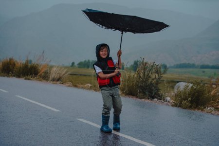 Junge steht auf der Straße und versucht, bei regnerischem Wind einen Regenschirm zu halten