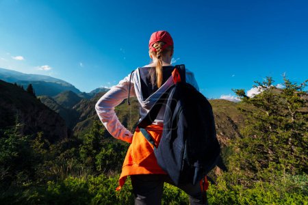 Photo for Young woman hiker with backpack stands on top of a mountain and looks at the valley - Royalty Free Image