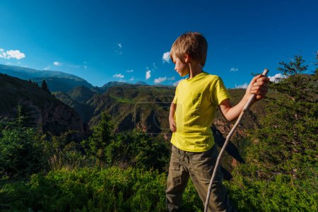 Foto de Chico excursionista con palo se para en la cima de una montaña y mira al valle - Imagen libre de derechos