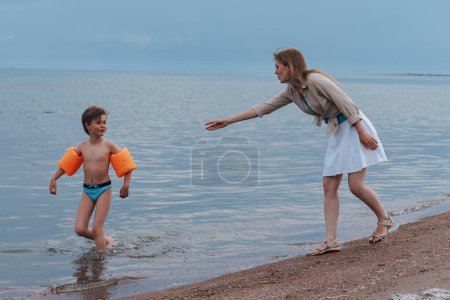 Foto de Madre e hijo travieso en la orilla del mar, madre llama al niño, pero se escapa - Imagen libre de derechos