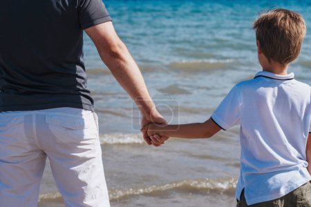 Téléchargez les photos : Père et fils debout sur la plage tenant la main - en image libre de droit