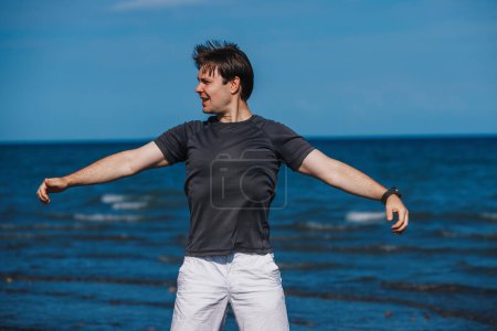 Téléchargez les photos : Un beau jeune homme se tient sur la plage par temps venteux et se réchauffe - en image libre de droit