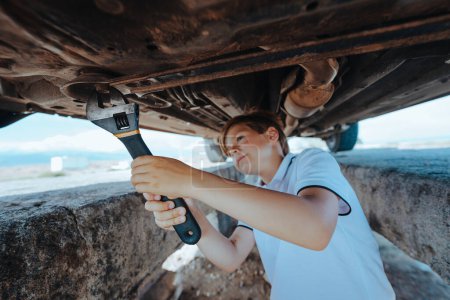 Téléchargez les photos : Garçon mécanicien automobile debout sous le fond de la voiture avec clé et réparation de voiture - en image libre de droit