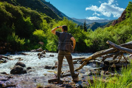 Foto de Joven excursionista parado en un desfiladero de montaña cerca del río y mirando hacia otro lado - Imagen libre de derechos