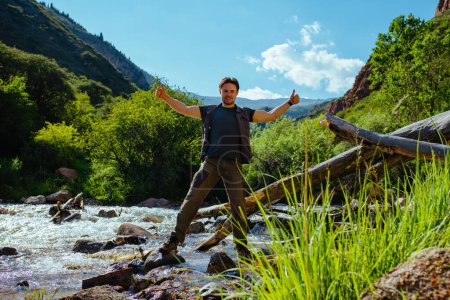 Foto de Joven excursionista se para junto a un arroyo de montaña y da un pulgar hacia arriba - Imagen libre de derechos