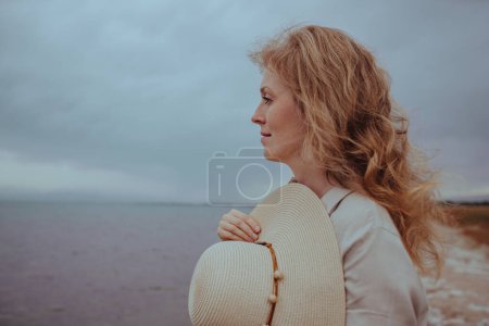Téléchargez les photos : Portrait de belle jeune femme avec chapeau sur la rive d'un lac par temps venteux - en image libre de droit