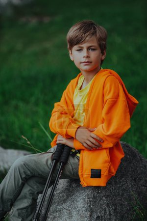 Téléchargez les photos : Garçon randonneur avec bâtons de trekking assis sur le rocher - en image libre de droit