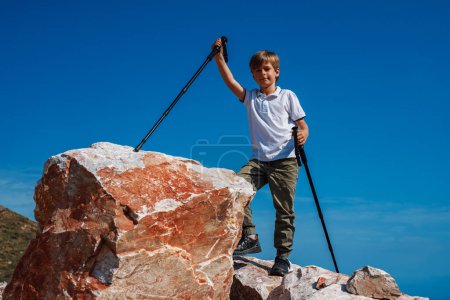 Foto de Niño excursionista con bastones de trekking de pie en la cima de una montaña - Imagen libre de derechos