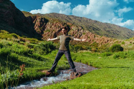 Photo for Man hiker standing and balancing on both sides of a mountain stream - Royalty Free Image