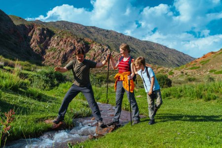 Téléchargez les photos : Parents randonnée avec leur fils à travers les montagnes ruisseau - en image libre de droit