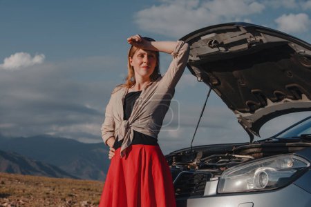 Téléchargez les photos : Fatigué jeune femme debout devant la voiture en panne sur fond de montagnes - en image libre de droit