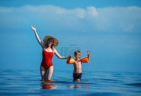 Téléchargez les photos : Joyeux jeune femme et son fils agitant les mains dans la mer - en image libre de droit