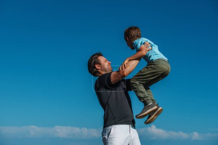 Foto de Feliz padre levanta a su hijo en lo alto sobre fondo azul del cielo - Imagen libre de derechos
