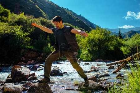 Photo for Young man hiker crosses mountain river at sunny summer day - Royalty Free Image