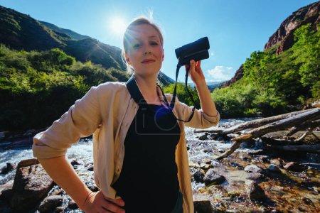 Photo for Young woman tourist with binoculars on the banks of a mountain river - Royalty Free Image