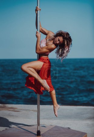 Téléchargez les photos : Jeune belle femme pole dance sur fond de mer et ciel - en image libre de droit